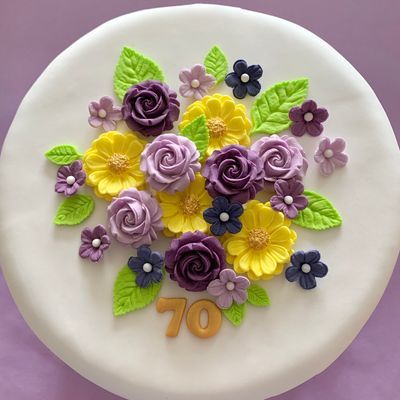 Iced cake topped with purple, lilac and yellow sugar roses and flowers
