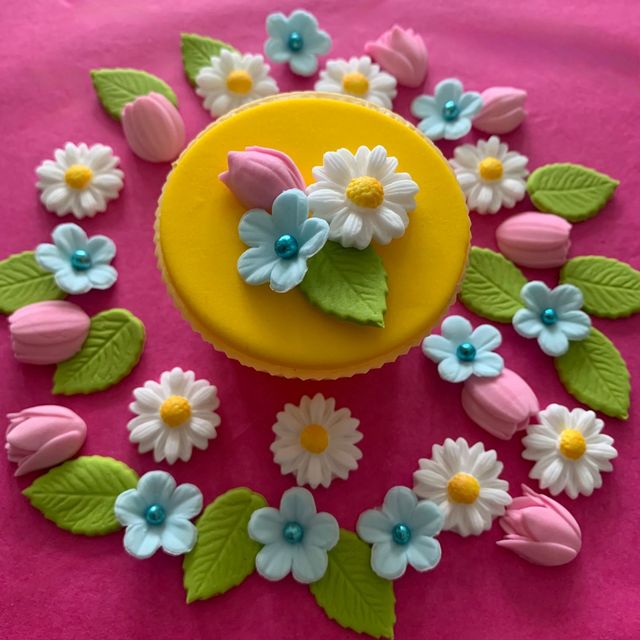 Small sugar daisies, pink tulips and blue flowers on a yellow cupcake